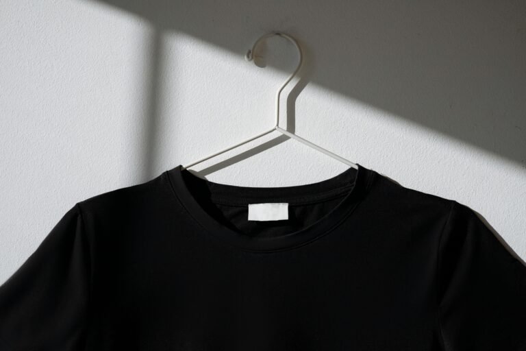 Black t-shirt hanging on a white hanger against a plain wall with a dramatic shadow effect.