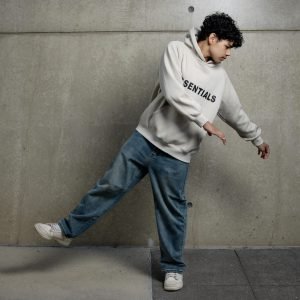 A teenager wearing a hoodie and jeans striking a fashionable pose indoors.